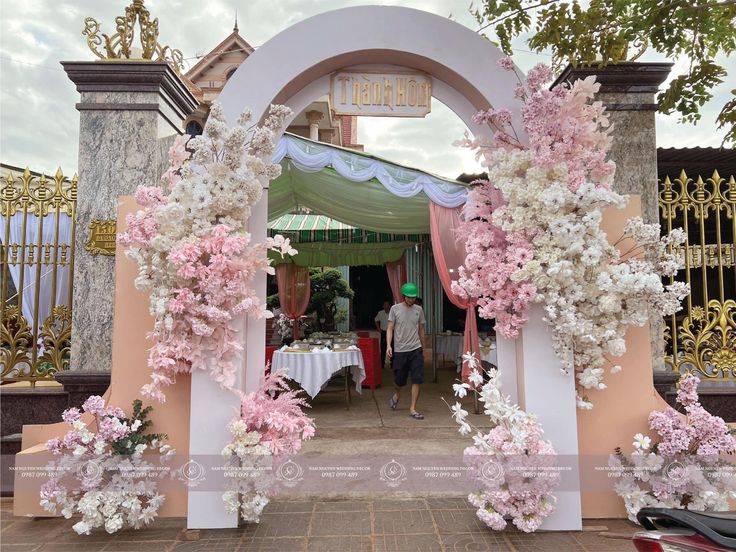 a man standing in front of a pink and white arch with flowers on it's sides