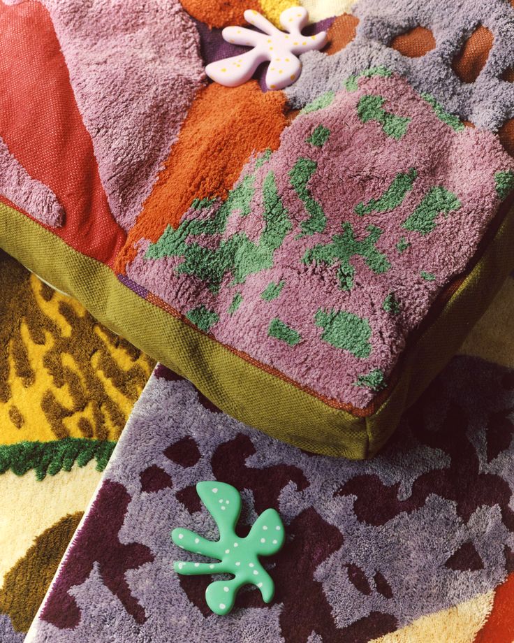 a green brooch sitting on top of a pile of purple and orange towels with flowers