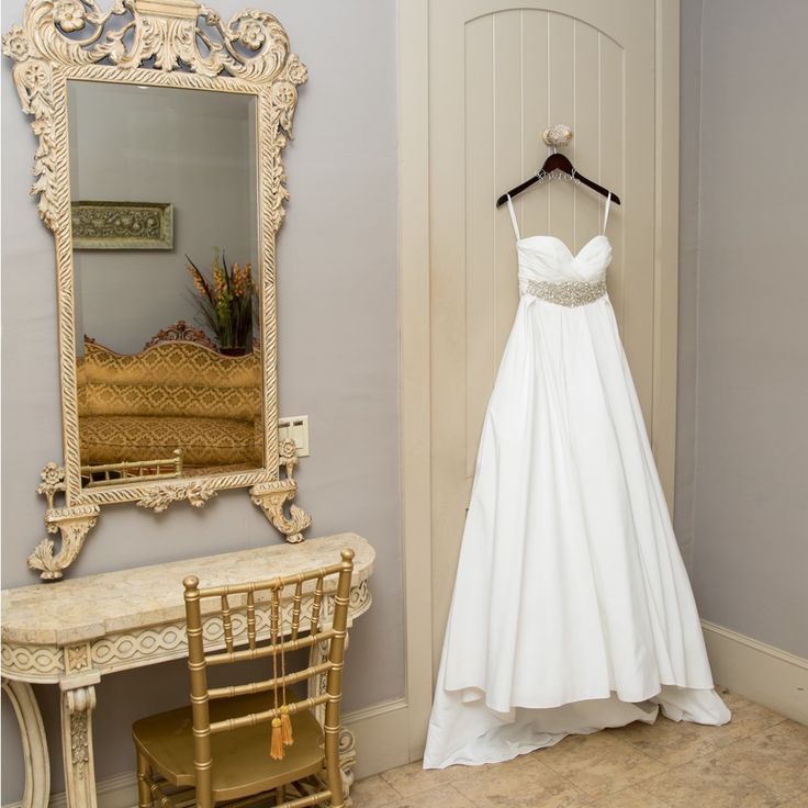 a wedding dress hanging on a hanger in front of a mirror and dressing table