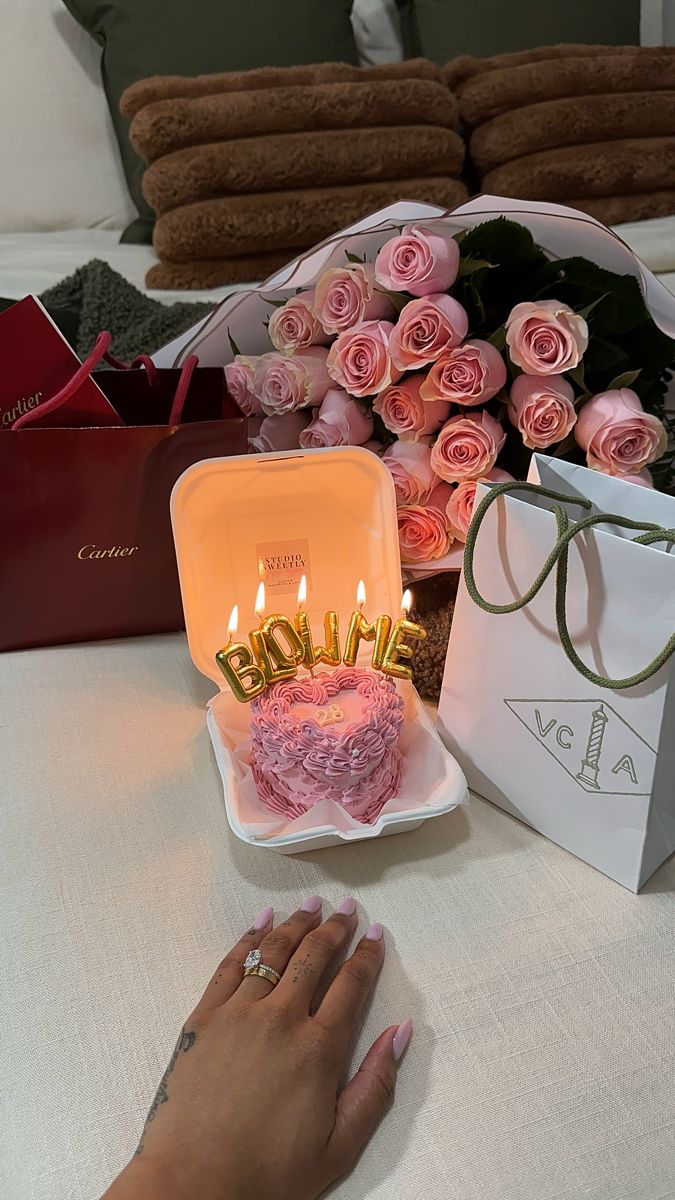 a birthday cake sitting on top of a table next to flowers and a bag with the word happy written on it