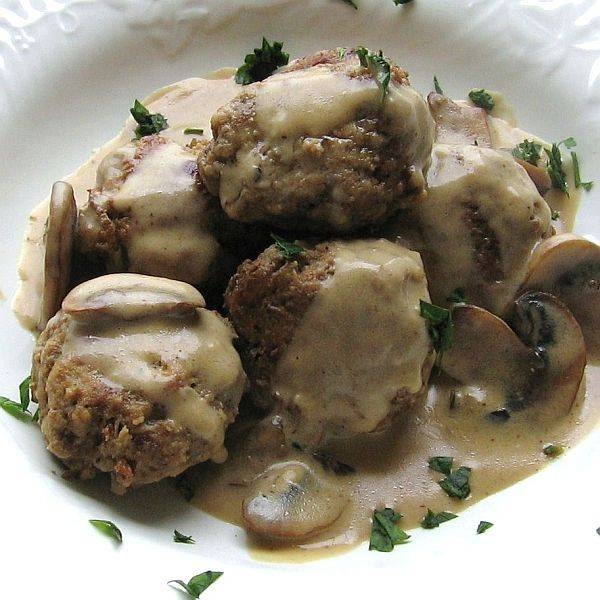 a white plate topped with meatballs covered in gravy and mushroom toppings