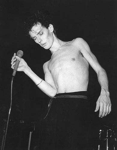 a shirtless man holding a microphone while standing in front of a microphone on stage