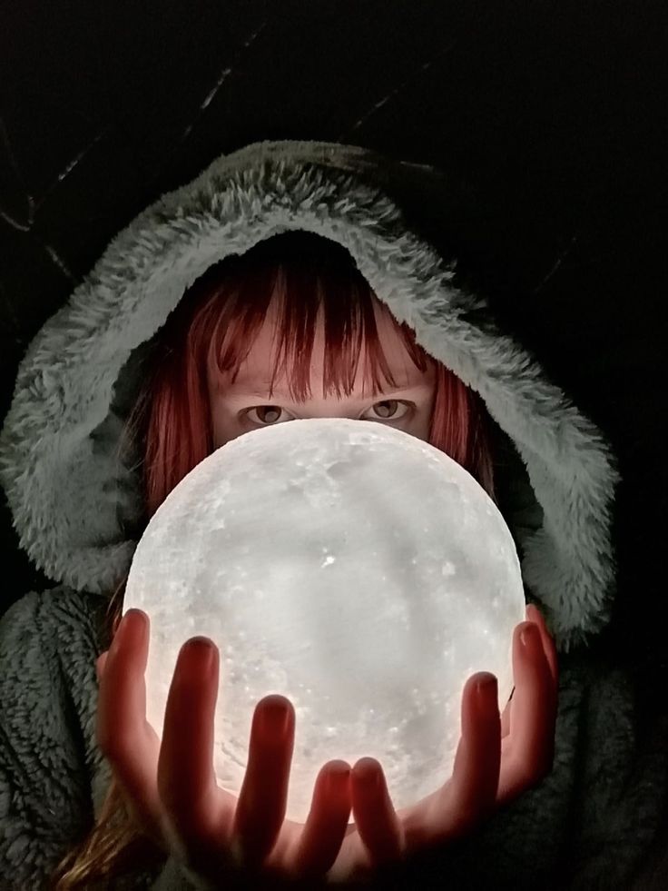 a woman holding a snowball in her hands with the light shining on her face