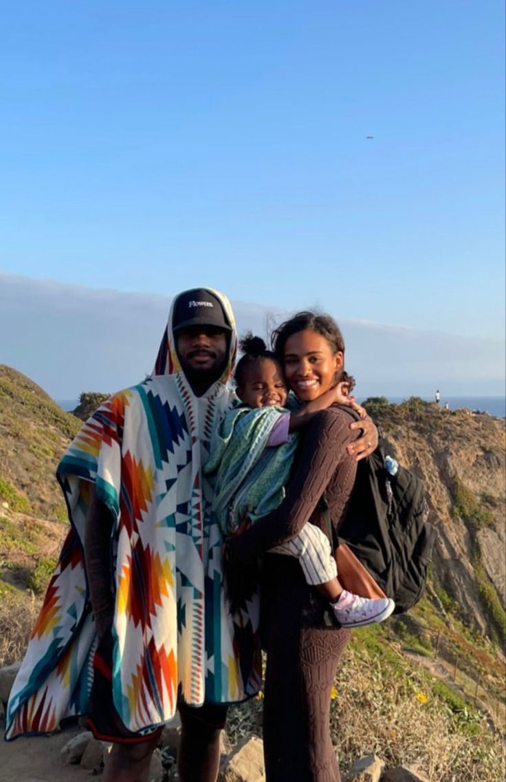 a man and woman standing on top of a mountain with a baby in their arms