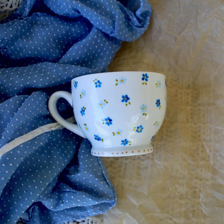 a blue and white cup sitting on top of a table next to a blue cloth