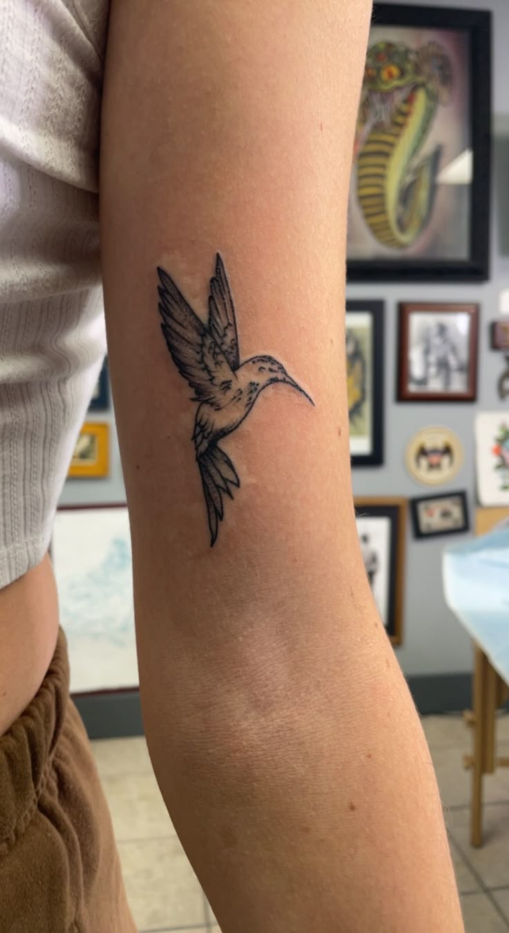 a small tattoo on the arm of a woman with a hummingbird flying above it