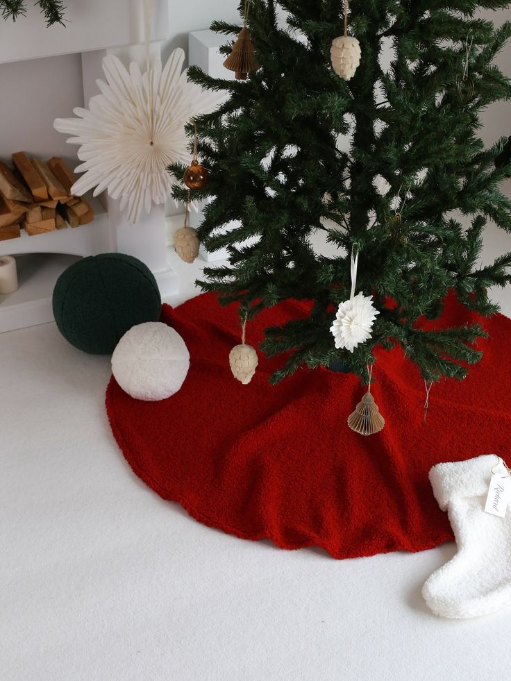 a small christmas tree in a red blanket next to white snowflakes and ornaments