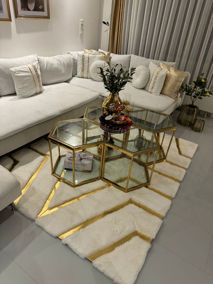 a living room filled with white couches and gold coffee table on top of a rug