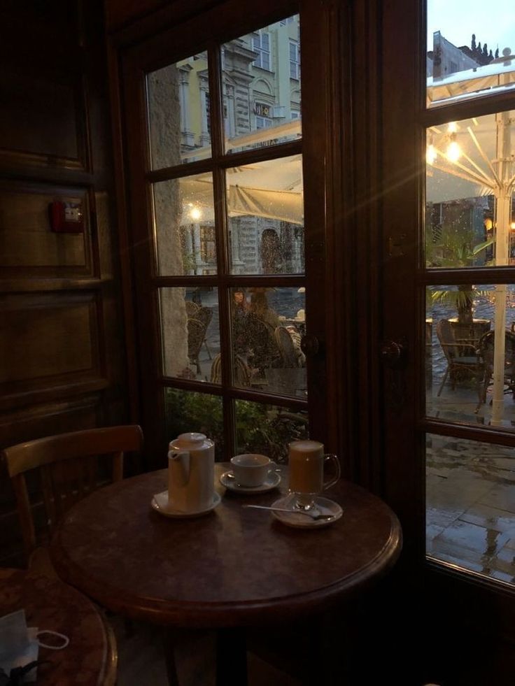 two cups of coffee sit on a table in front of an open window