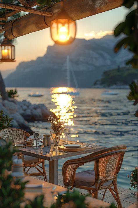 an outdoor dining area overlooking the water at sunset with lanterns hanging from the ceiling and table set for two