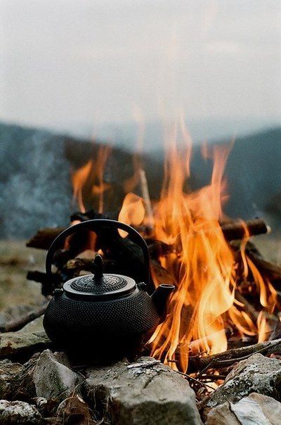 a tea kettle sitting on top of a pile of rocks next to a campfire