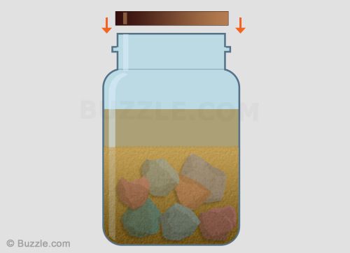 a glass jar filled with rocks sitting on top of a floor next to a wall