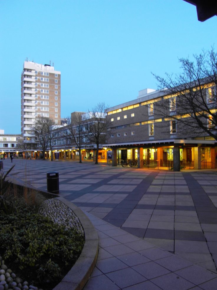 an empty plaza with buildings in the background at dusk, as seen from across the street