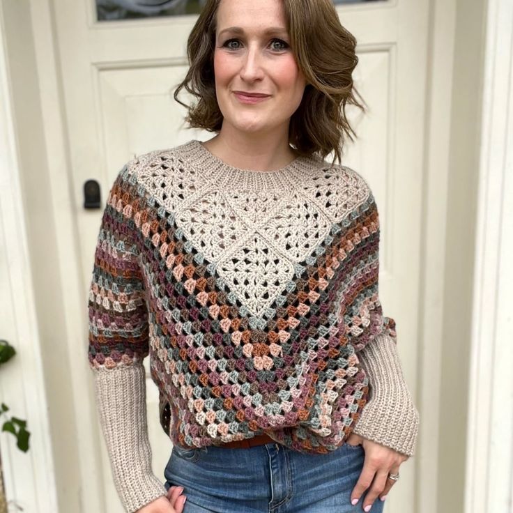 a woman standing in front of a door wearing a crocheted sweater and jeans