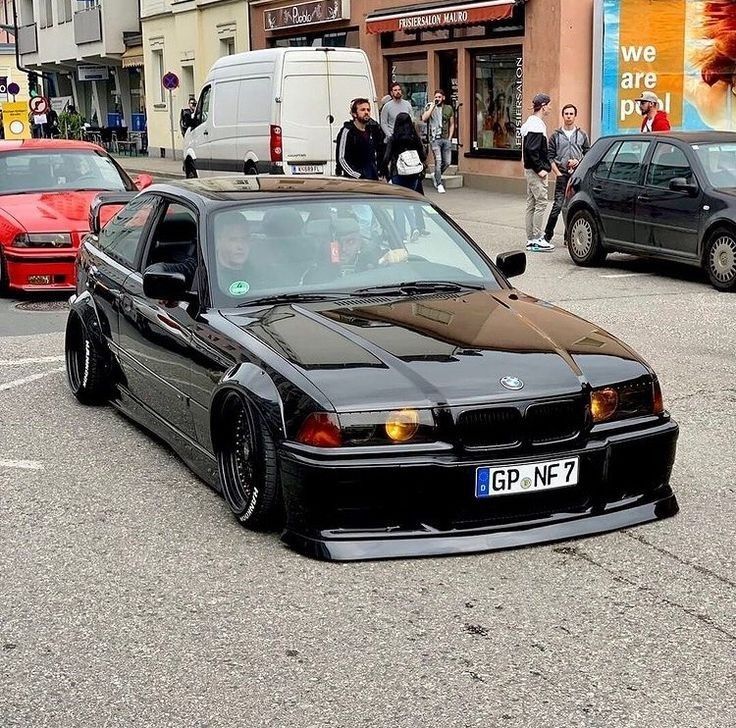 a black car is parked on the side of the road in front of other cars