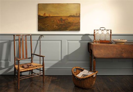 two chairs and a table with a basket on it in front of a painting hanging on the wall