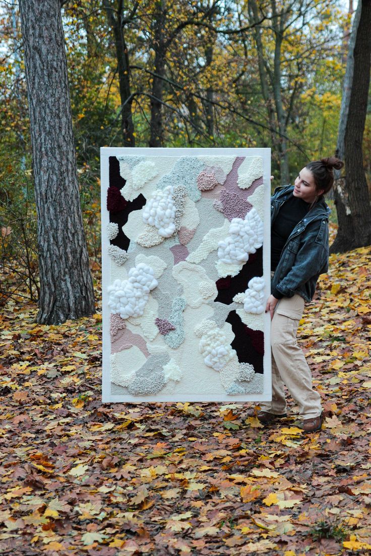 a woman standing next to a large quilt in the woods with leaves on the ground