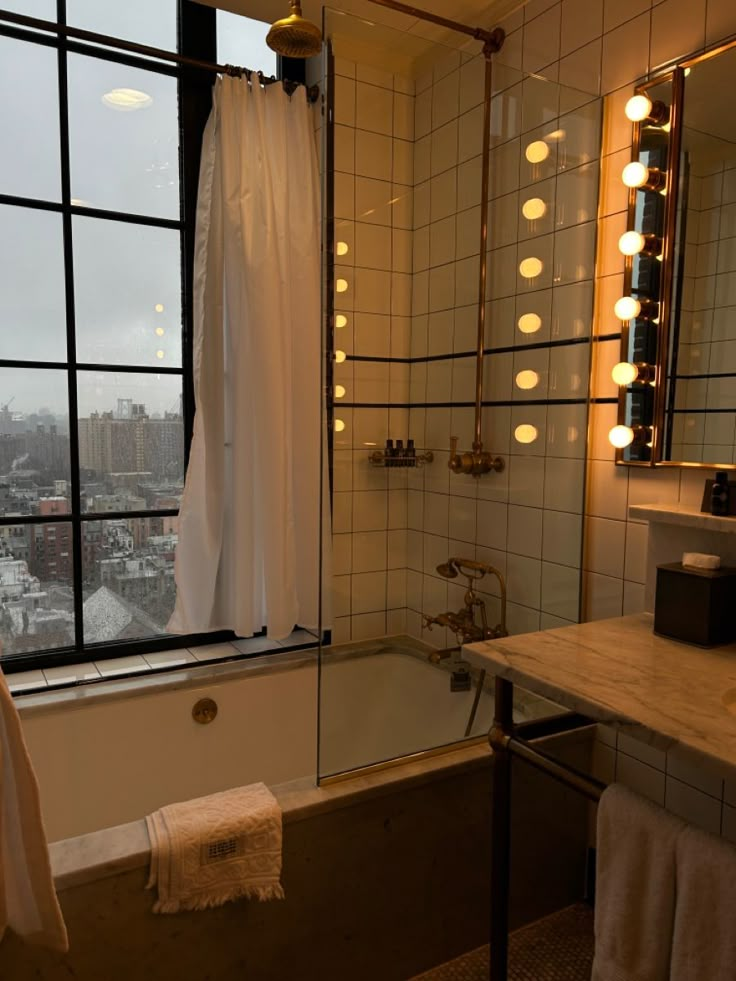 a bath tub sitting next to a bathroom sink under a window with lights on it