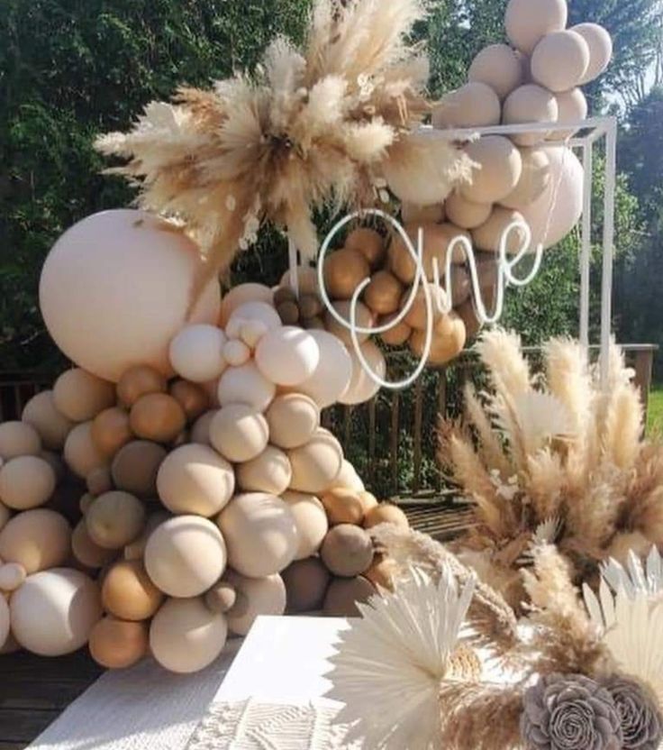 a table topped with lots of white and brown balloons covered in feathers next to trees