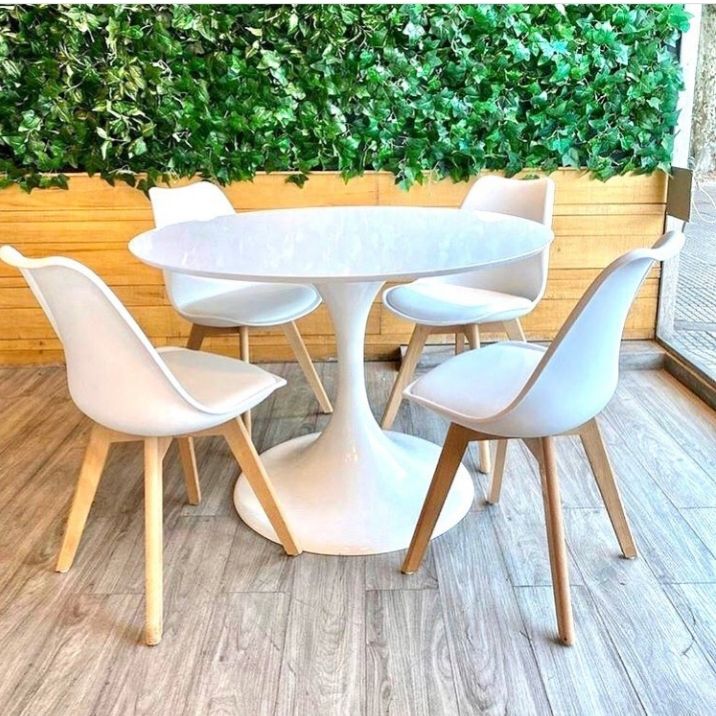 a white table and four chairs in front of a wall with green plants on it