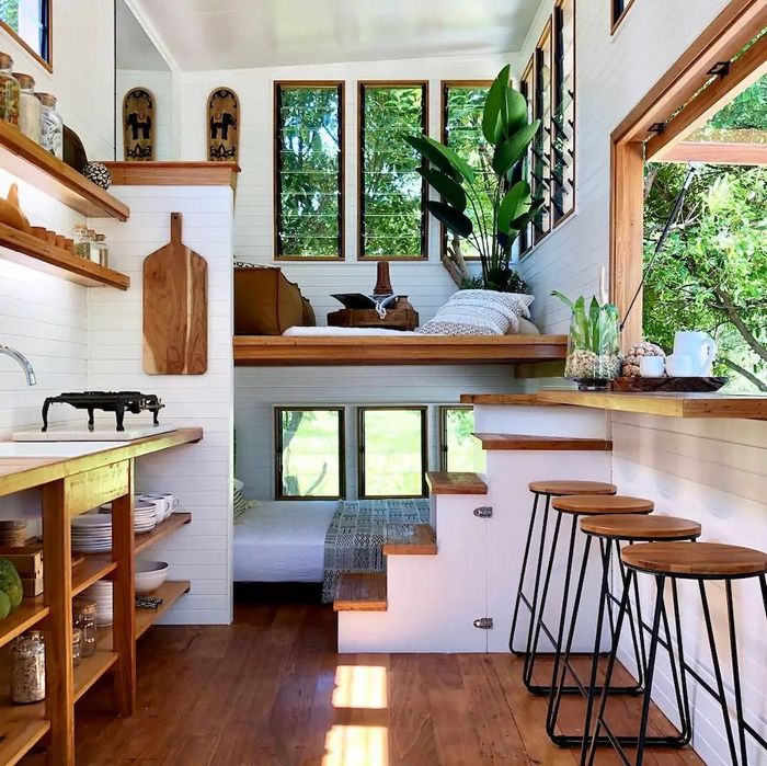 the interior of a tiny house with wood floors and shelves on each side, along with three stools