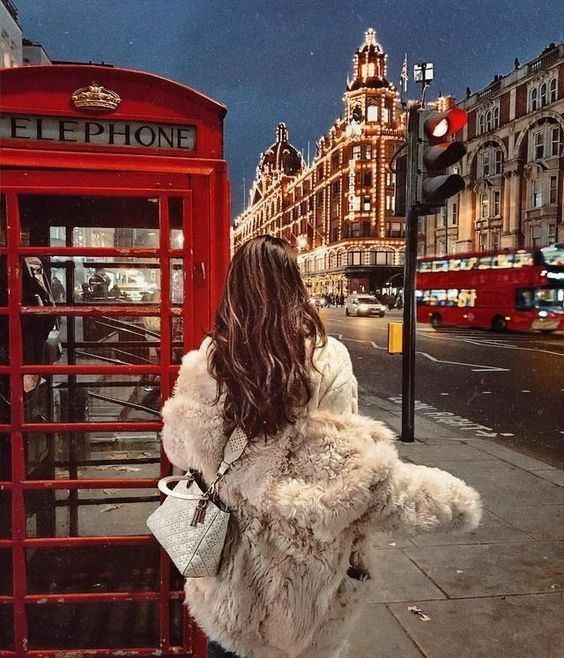 a woman is standing in front of a red phone booth on the side of the street