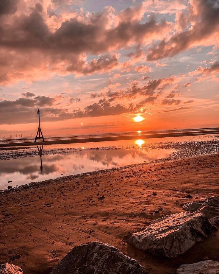 the sun is setting at the beach with rocks in the foreground and clouds in the background