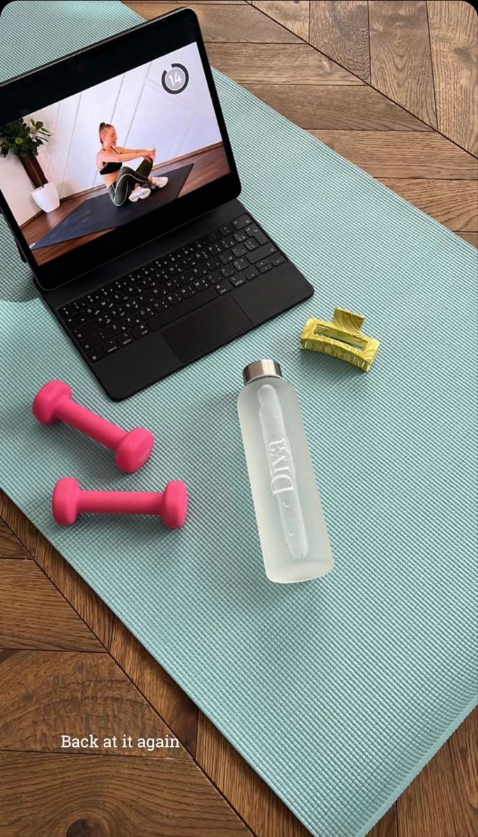 an open laptop computer sitting on top of a yoga mat next to two pink dumbs