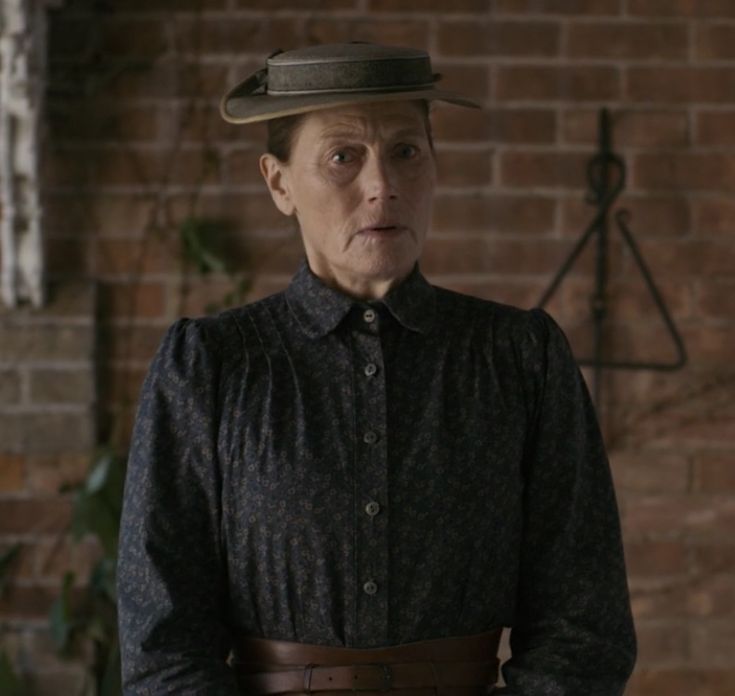 an older woman wearing a hat standing in front of a brick wall