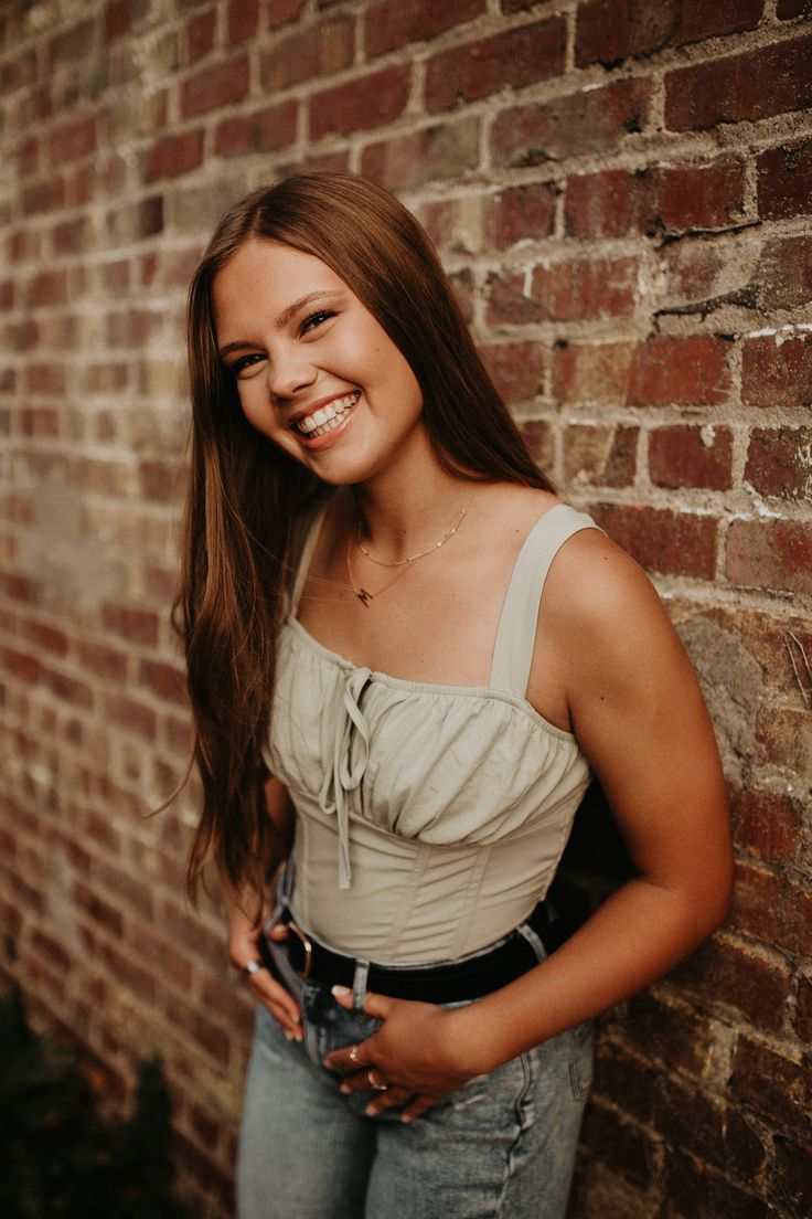 a woman standing in front of a brick wall with her hands on her hips and smiling at the camera