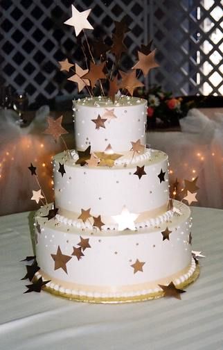 a three tiered cake with gold stars on the top and white frosting, sitting on a table