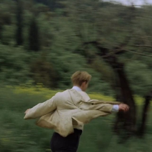 a man is running in the grass with his coat over his shoulders and jacket on