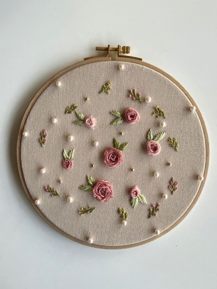 a close up of a embroidery on a white surface with pink flowers and pearls in the hoop