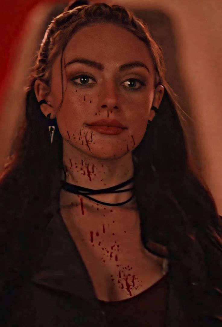 a woman with blood all over her face and neck, standing in front of a red wall