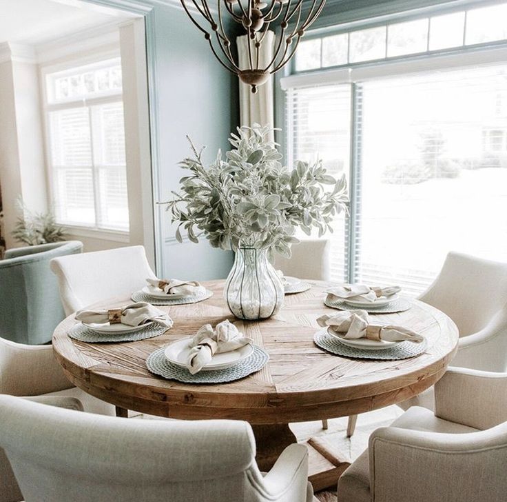 a dining room table with white chairs and flowers in a vase on the centerpiece