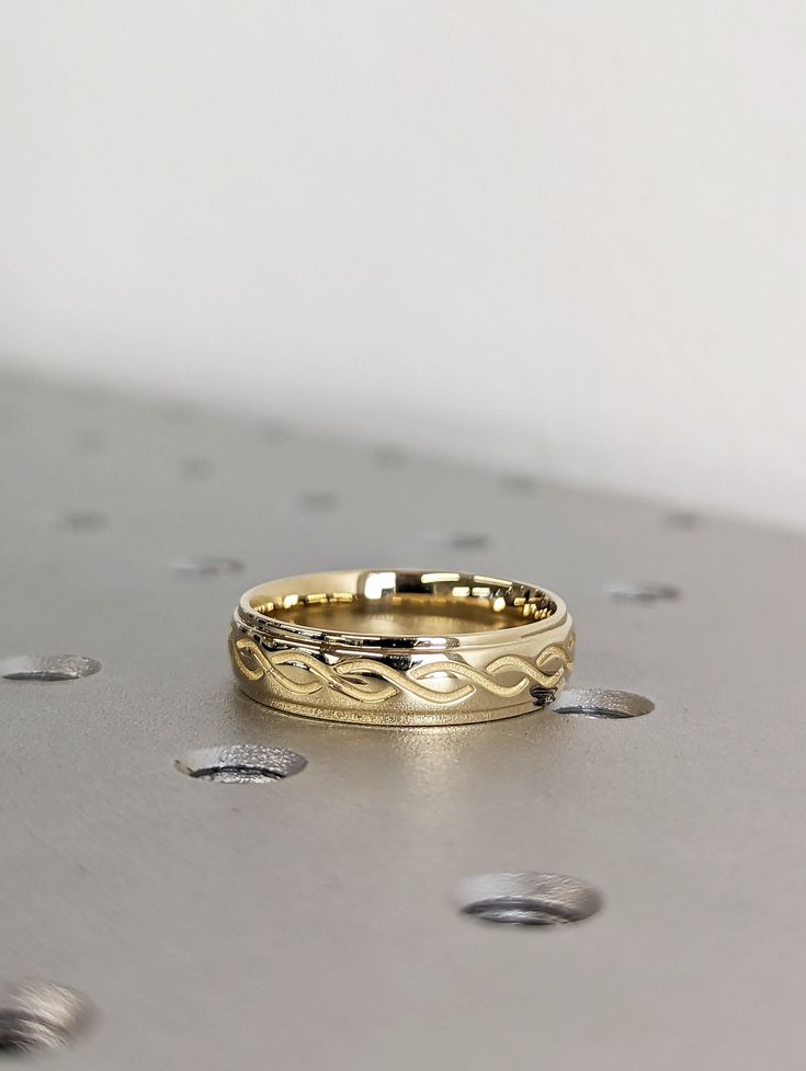 two gold wedding bands sitting on top of a metal surface with drops of water around them