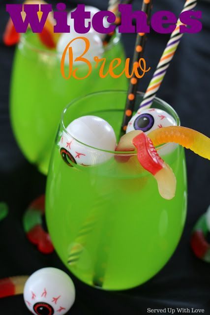 two glasses filled with green liquid and halloween decorations on the rim, sitting next to each other