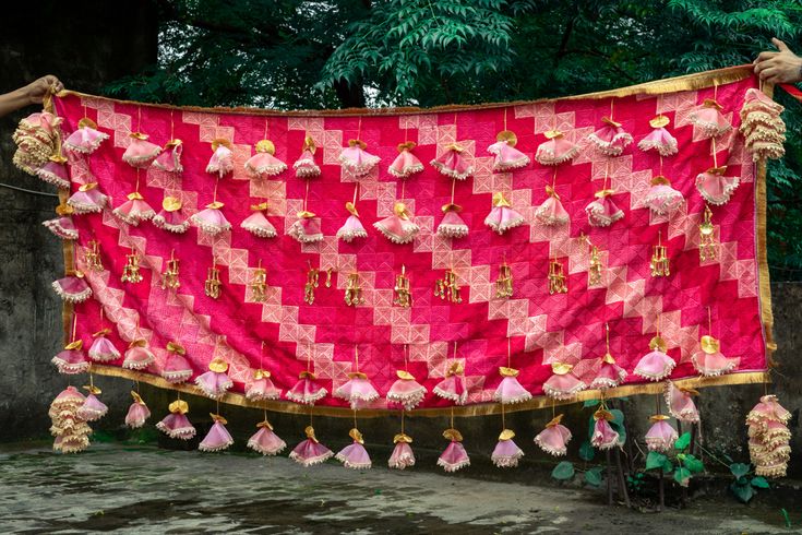 a red and pink blanket with tassels hanging from it's sides in front of some trees