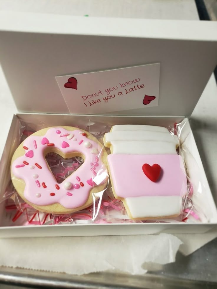 two decorated cookies in a white box with pink frosting