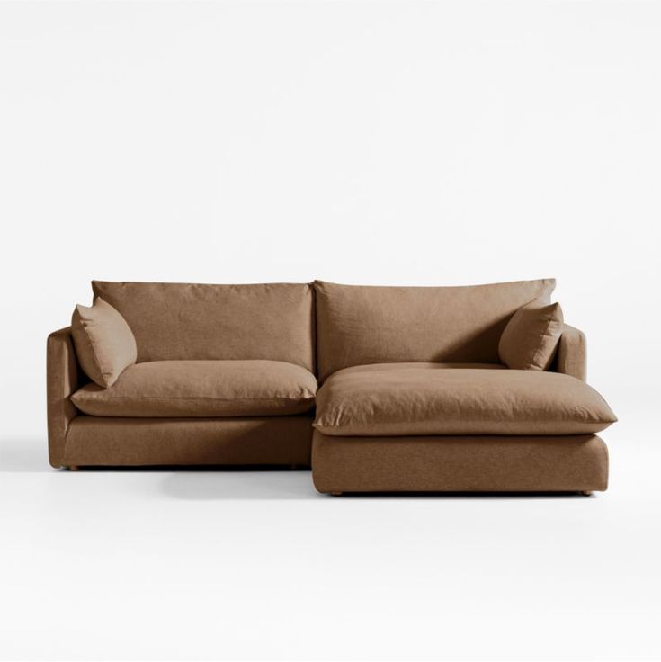 a brown couch with pillows on it sitting in front of a white wall and floor