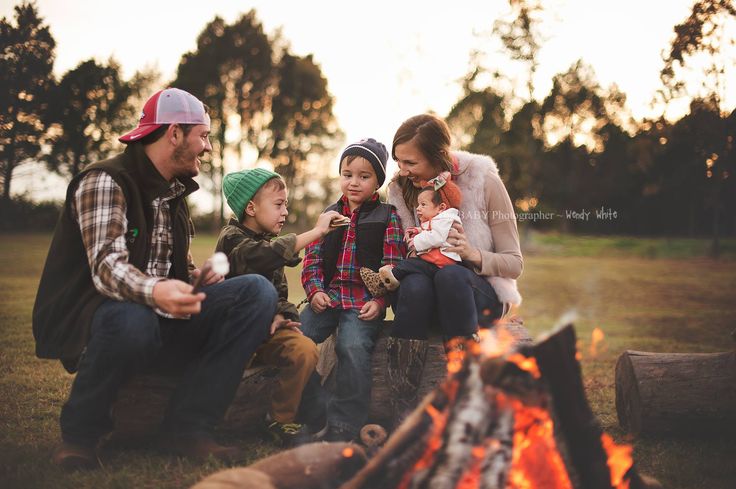 a group of people sitting around a campfire in the grass with a baby on their lap