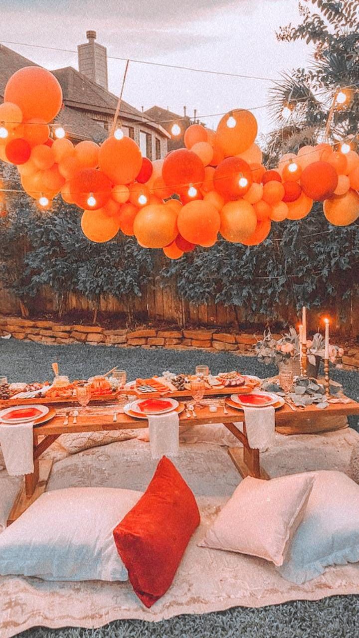 an outdoor table set up for a party with orange balloons hanging from the ceiling over it