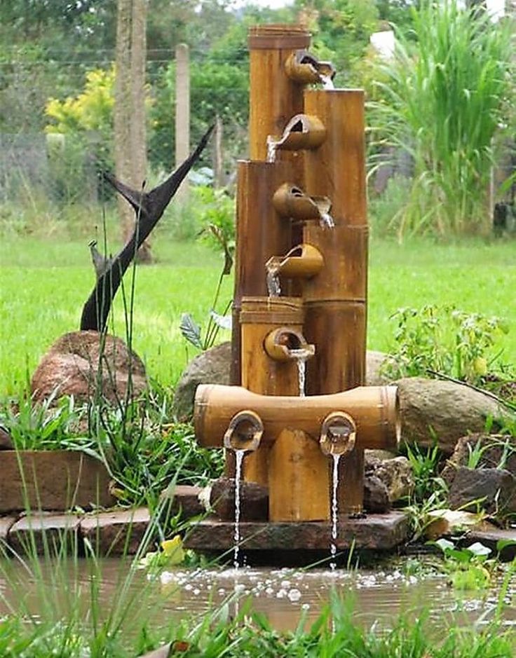 a water fountain made out of bamboo sticks and other items in a garden with green grass