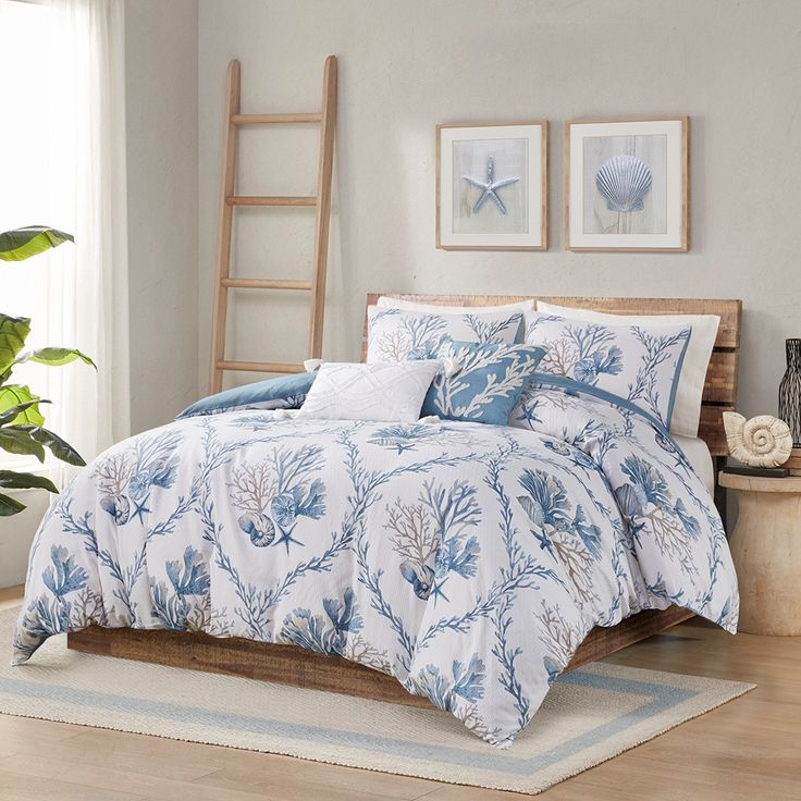 a bed with blue and white comforters in a room next to a ladder, potted plant and pictures on the wall