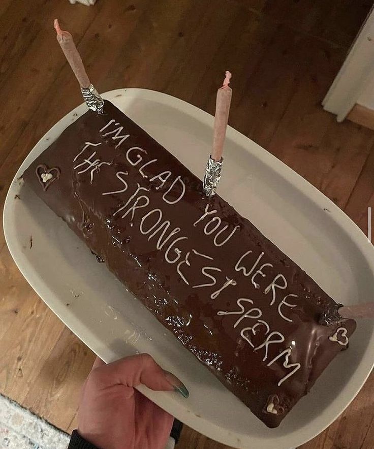 a person holding a cake with writing on it and two lit candles sticking out of the top