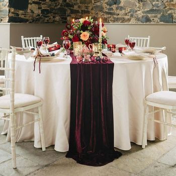 the table is set with white linens, red and orange flowers, candles, and wine glasses