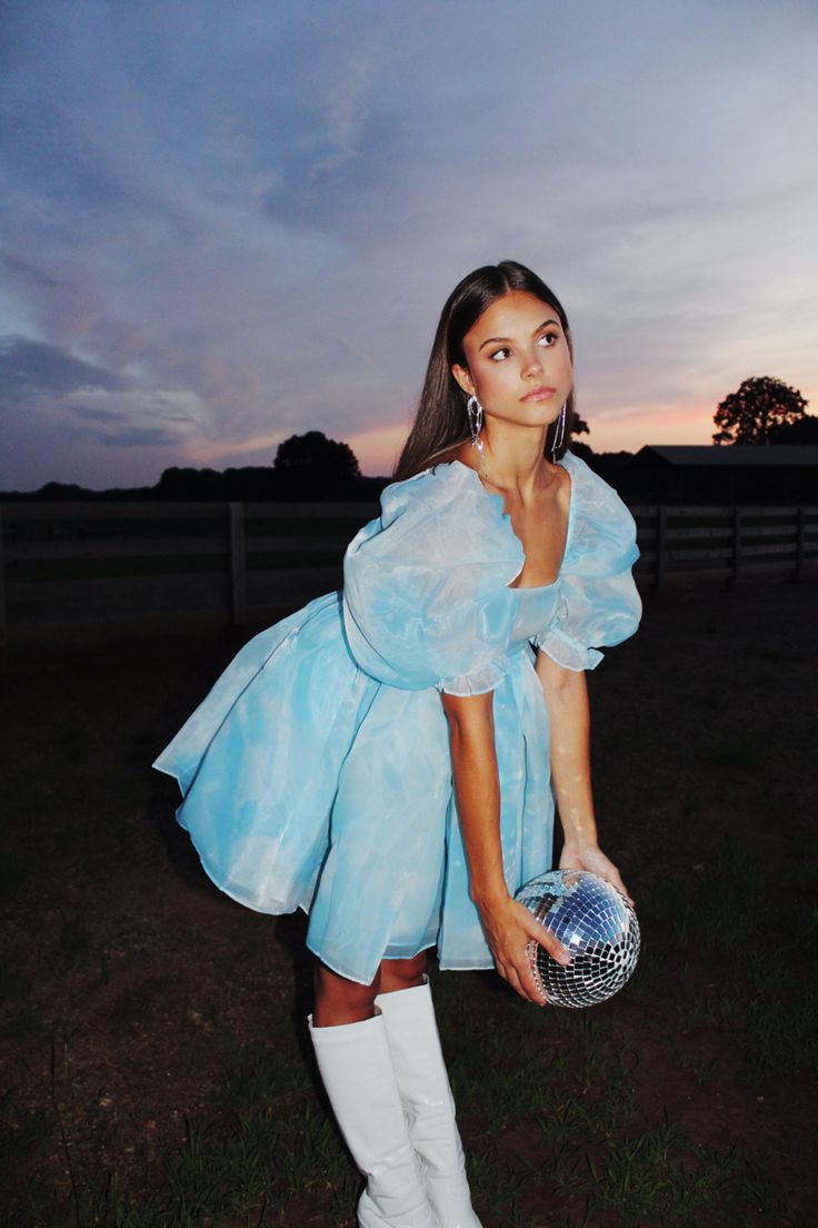 a woman in a blue dress and white boots holding a disco ball with her hands