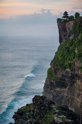 an ocean cliff with a small hut on it's top and waves crashing in the water