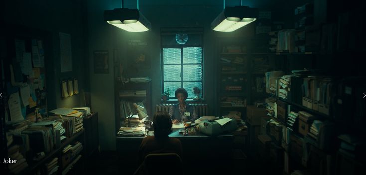 a person sitting at a desk in a dark room with lots of books on the shelves