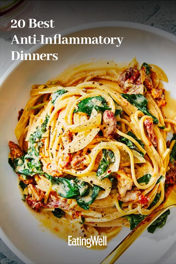 a white plate topped with pasta covered in sauce and spinach next to a fork